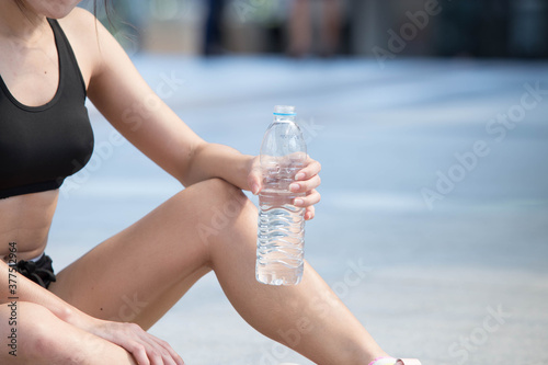 Young sport woman sit and hold a plastic bottle of water after work out in a city