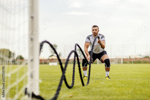 Soccer player doing exercises on the field. He is doing exercises with battle ropes.