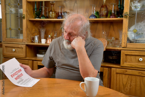 Frustrated old man sitting and reading the eviction notice he just received.. photo