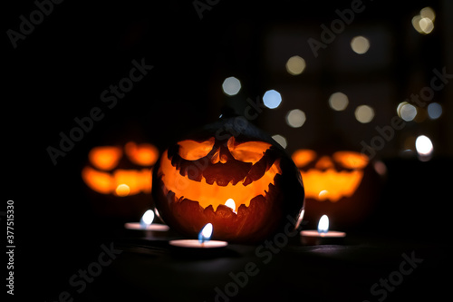 Halloween pumpkin jack o lantern with candles in the dark. Glowing eyes and mouth. Against the background of blurry jack-o'-lanterns and pumpkins with bokeh. 