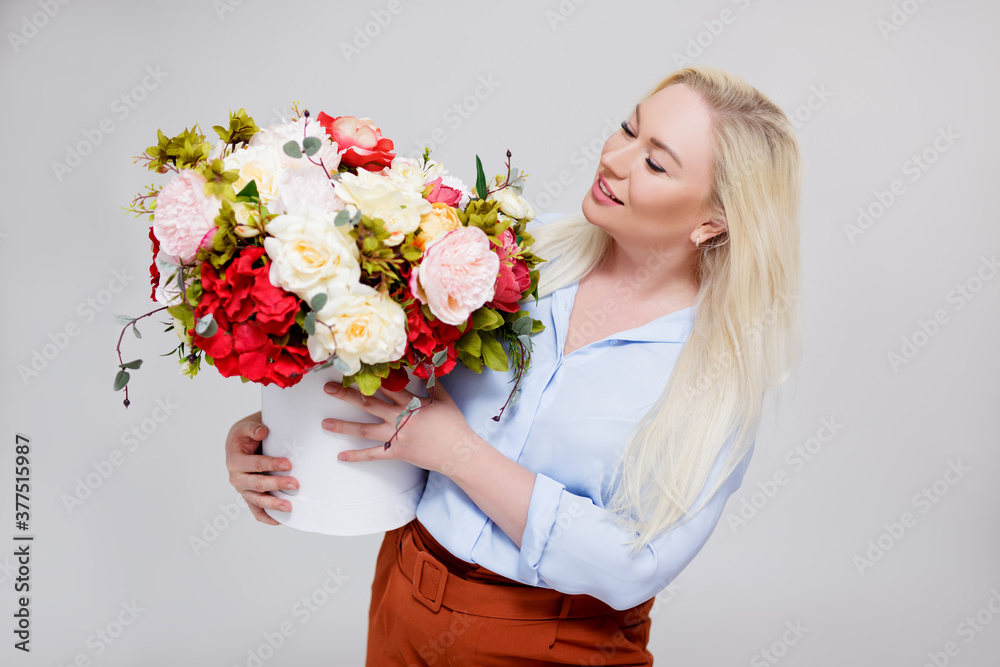 portrait of beautiful and elegant plus size blonde woman holding box with summer flowers over gray portrait of beautiful and elegant plus size blonde woman holding box with summer flowers over gray