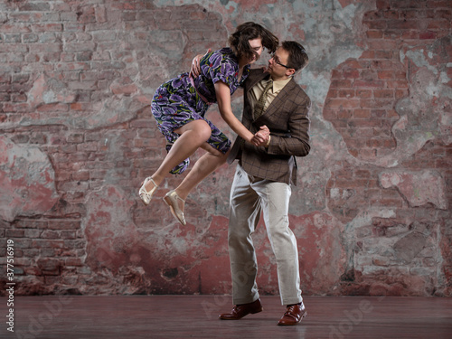young couple dancing swing indoors in a studio against an old brick wall, performing a jump