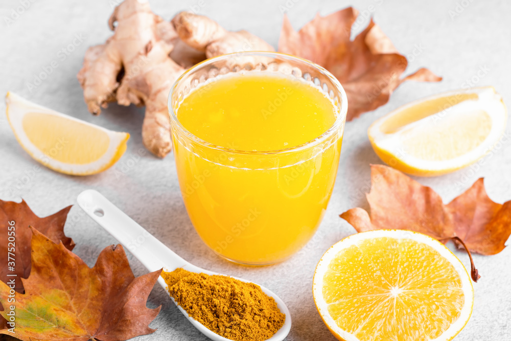 Immune boosting drink with citrus fruits, ginger, turmeric. Drink or smoothie with yellow fall leaves for autumn or virus season on neutral beige background Immune boosting drink with citrus fruits, ginger, turmeric. Drink or smoothie with yellow fall leaves for autumn or virus season on neutral beige background