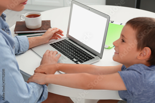 Fotografía Little boy bothering mother with laptop at work in kitchen, closeup