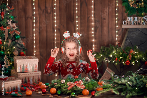 Little girl decorating coniferous wreath near Christmas tree in the decorative interior. Christmas and New Year photo.