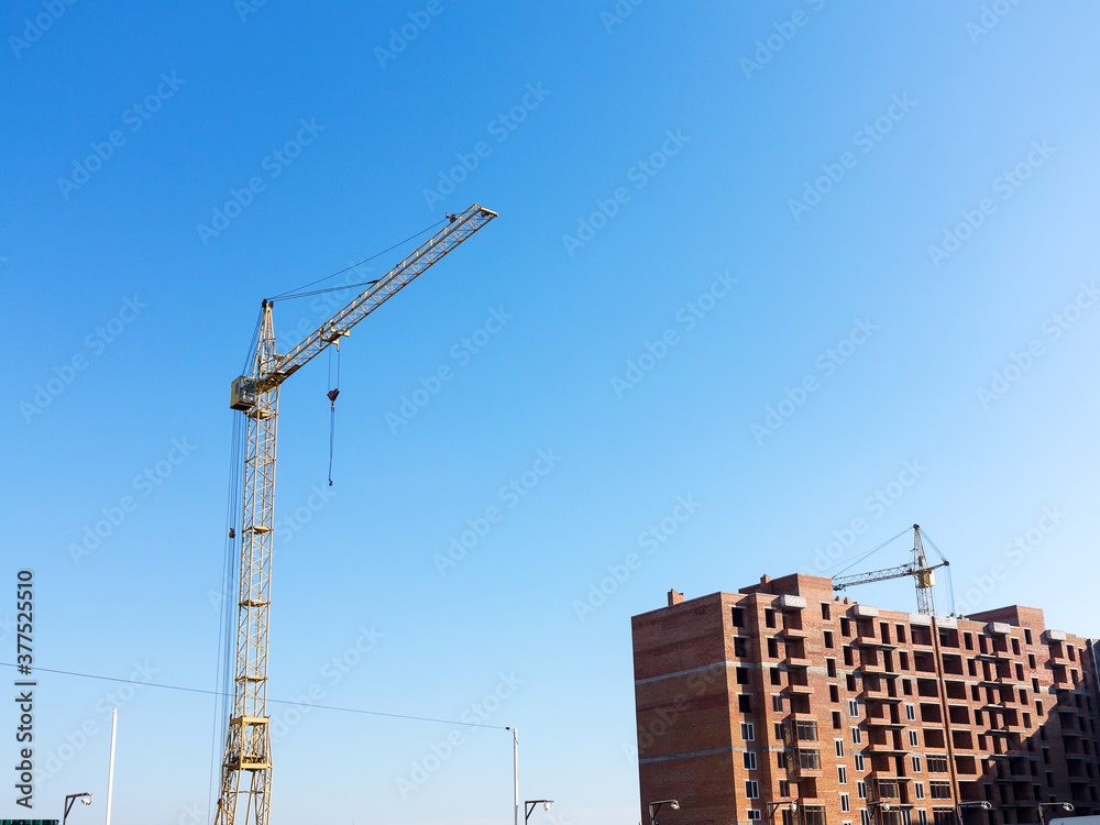 Crane near the brick high-rise building under construction against the blue sky, modern construction