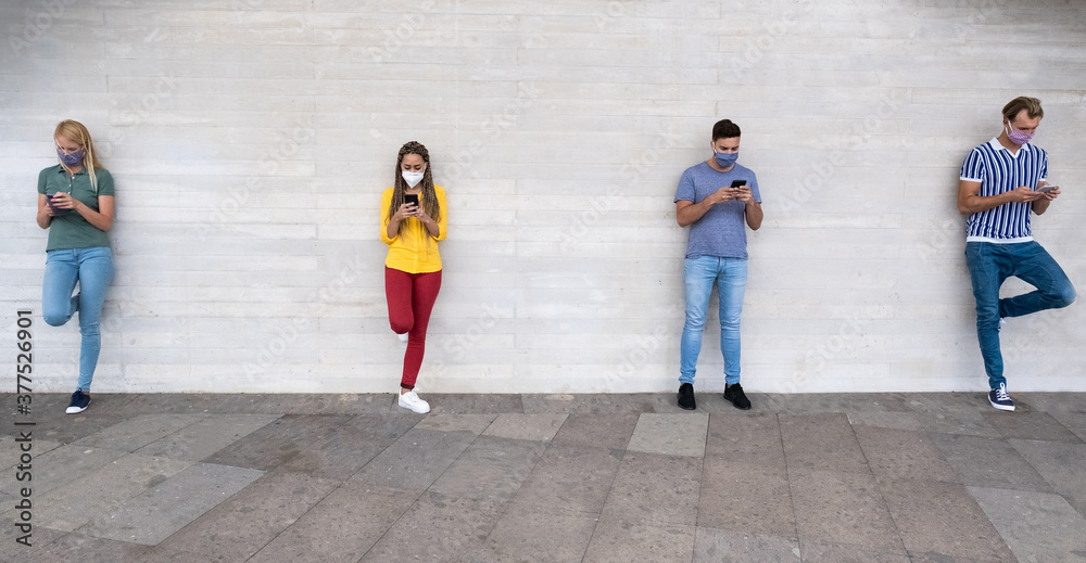Young multiracial people standing in a line with social distance and looking at smartphone while wearing protective face mask - Coronavirus lifestyle Young multiracial people standing in a line with social distance and looking at smartphone while wearing protective face mask - Coronavirus lifestyle