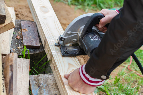 Sawing a wooden Board with an electric grinder. A man saws wooden planks using a fast-rotating metal saw blade.