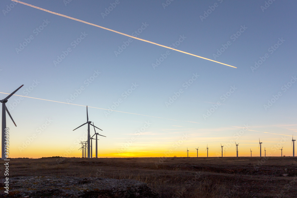 Obraz premium Wind Turbines at Dusk. Landscape sunset with windmills. Renewal source of electricity. Wind turbines field new technology for clean energy on mountain, sunset view with colorful twilight on sky