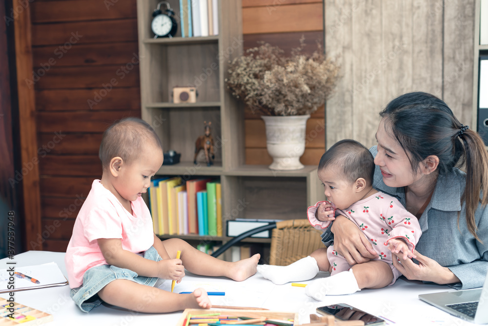 Busy woman trying to work while babysitting two daughter. Young beautiful Asian mother holding little baby on lap while another daughter playing around her. Working women with multitasking. Busy woman trying to work while babysitting two daughter. Young beautiful Asian mother holding little baby on lap while another daughter playing around her. Working women with multitasking.
