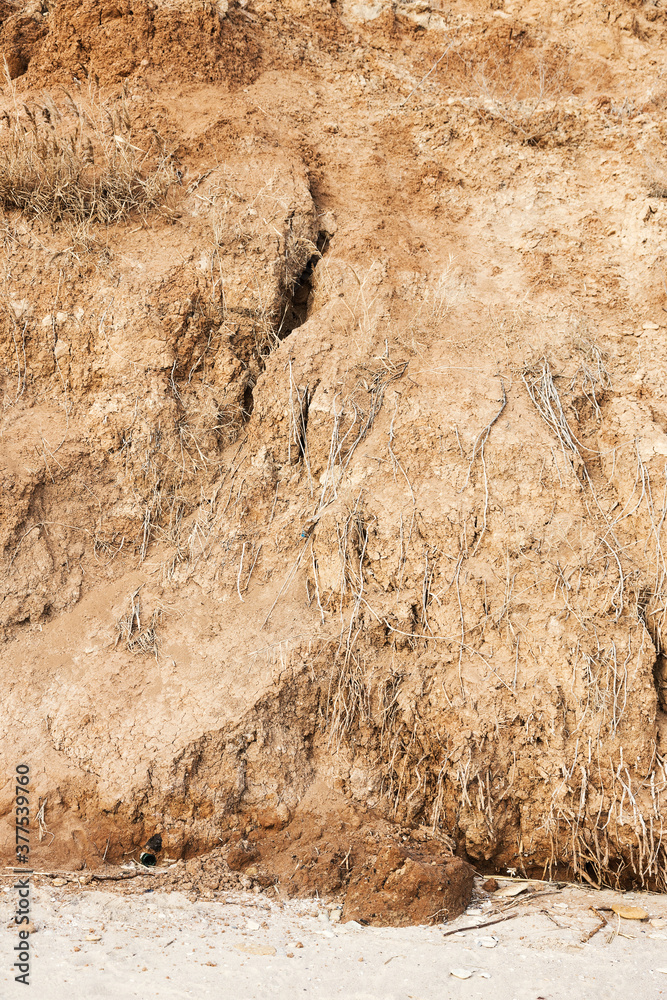 Obraz premium Background of mountain landslide in an environmentally hazardous area. Large cracks in the ground, the descent of soil layers, coquina. Deadly risk of coastal collapse