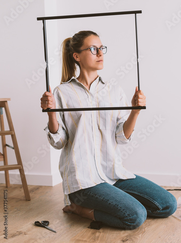 Girl in glasses and jeans sitting on the floor and holding black square in her hands. Room repairs, blank picture. 