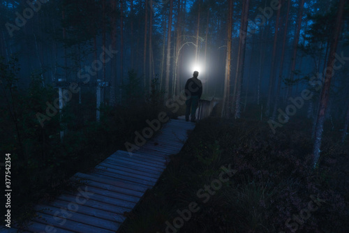 Person with headlamp looking in forest on boardwalk with fog