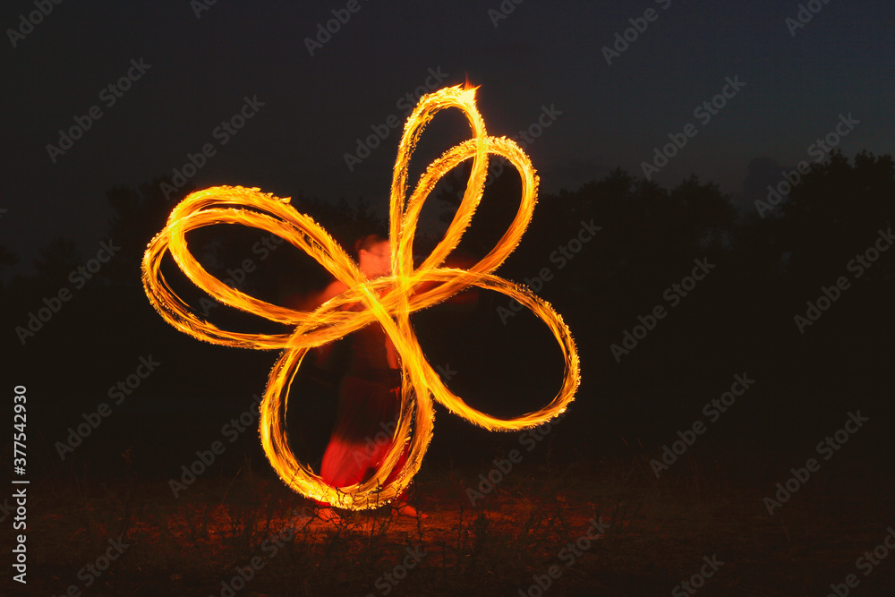 Fire dancer drawing figures by fire at night. Fakir woman turns fire in the field at night