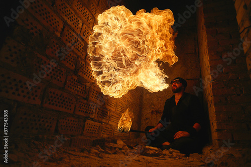 Male fakir blowing out fire in an abandoned building at night. Fire performer blowing out fire close-up.