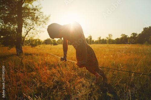 Young man walking on slackline in the meadow at sunset.