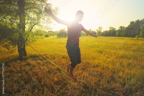  Young man walking on slackline in the meadow at sunset. photo