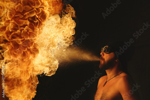 Male fakir blowing out fire in an abandoned building at night. Fire performer blowing out fire close-up. photo