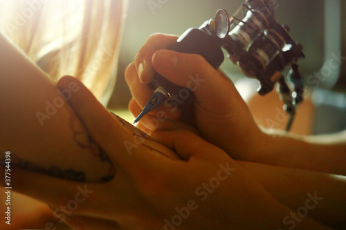 Close-up of a tattooist making a tattoo on the hand of a young woman. Tattoo master tattooing on the a girl arm.