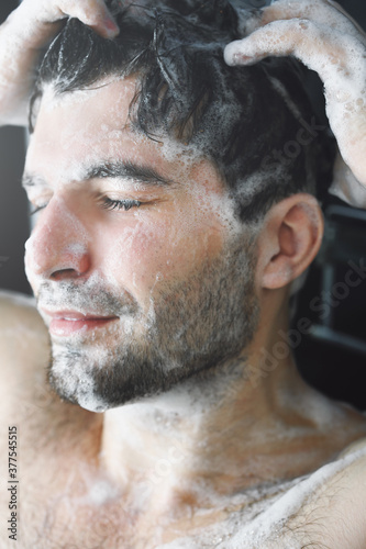 Young brunette man washes his hair in the shower
