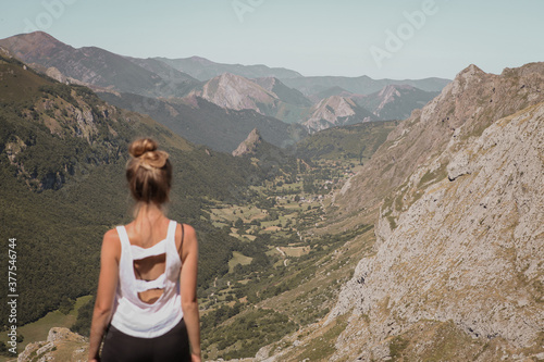 Young woman standing on the top of the mountain watching the beautiful landscape of Somiedo natural park in Asturias, Spain, mountain valley