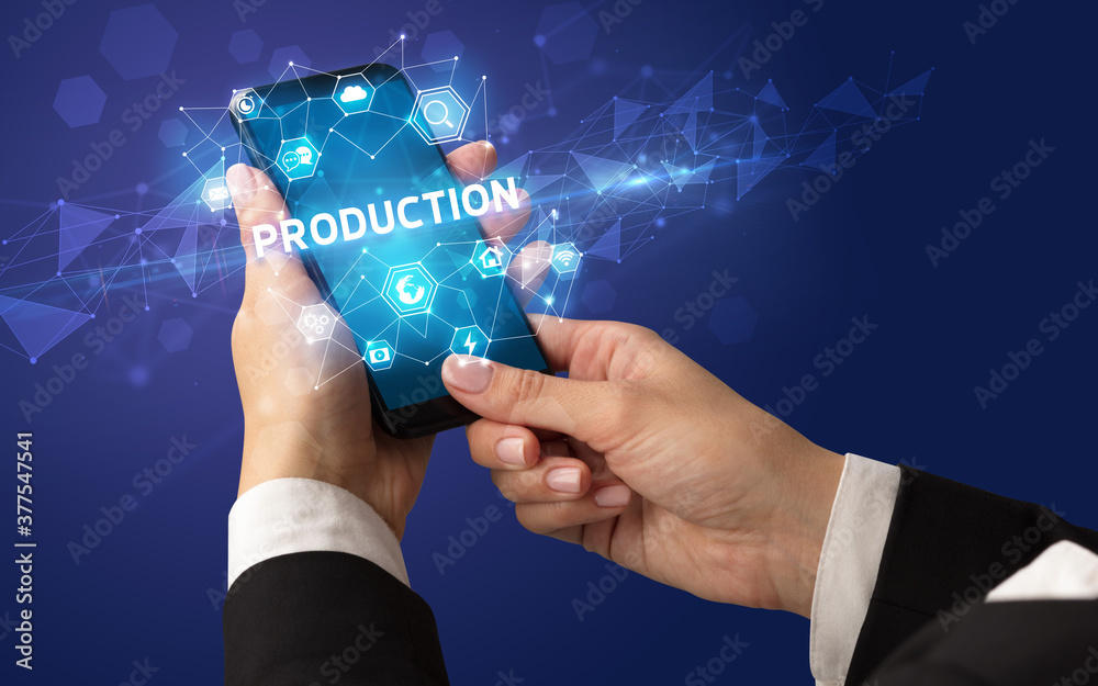 Female hand holding smartphone with PRODUCTION inscription, modern technology concept Female hand holding smartphone with PRODUCTION inscription, modern technology concept