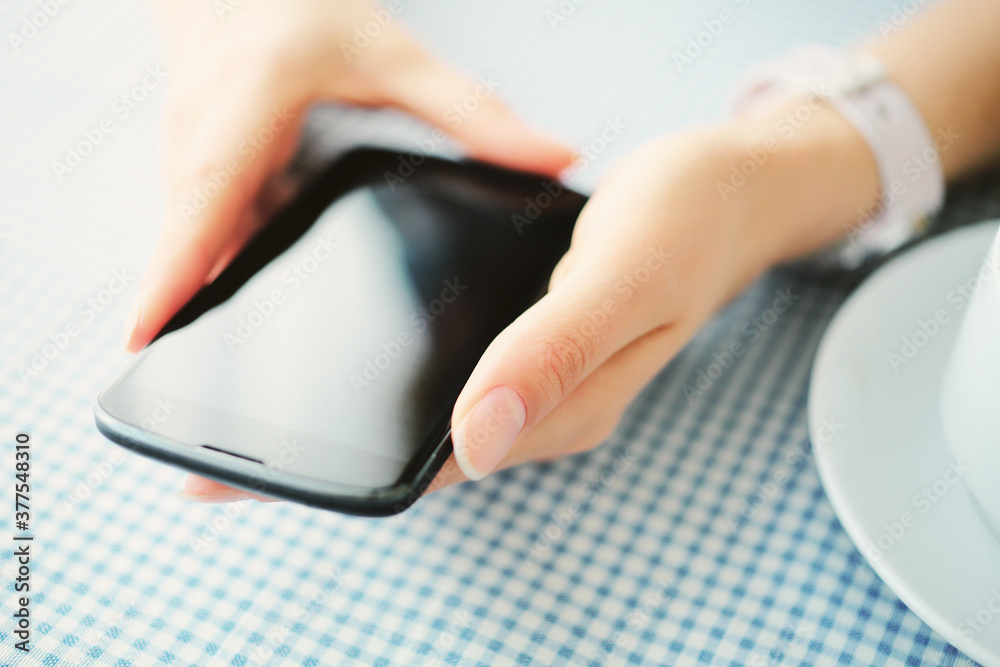 Fototapeta premium Closeup of hands of a young caucasian woman using smartphone in cafe.