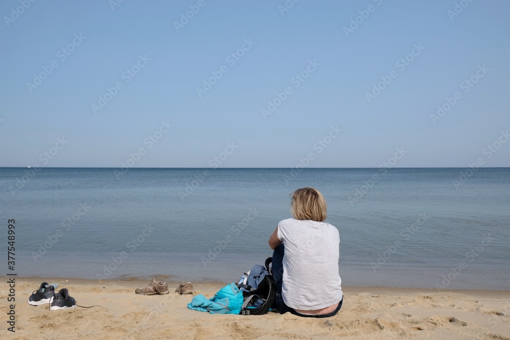 Woman sitting on the sand at the beach of the Baltic Sea on a sunny summer day, Sobieszewska Island, Poland