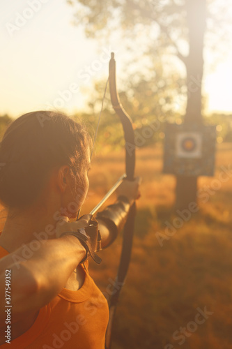 Obraz na płótnie Young Caucasian female archer shooting with a bow in a field at sunset