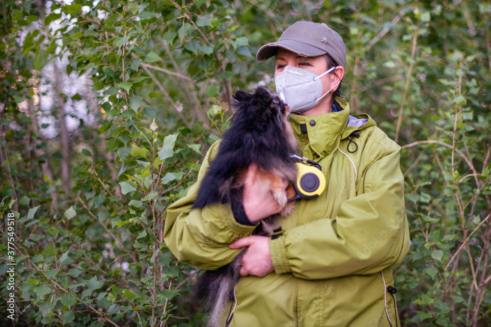 A girl wearing respirator mask walking with a Pomeranian dog in the forest protecting from COVID-19.