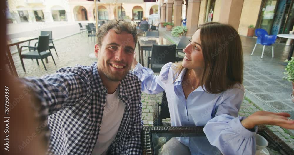 An young carefree happy romantic couple in love is making selfie or technology video call with smartphone to friends or family while enjoying a breakfast together in city center cafeteria on a weekend An young carefree happy romantic couple in love is making selfie or technology video call with smartphone to friends or family while enjoying a breakfast together in city center cafeteria on a weekend