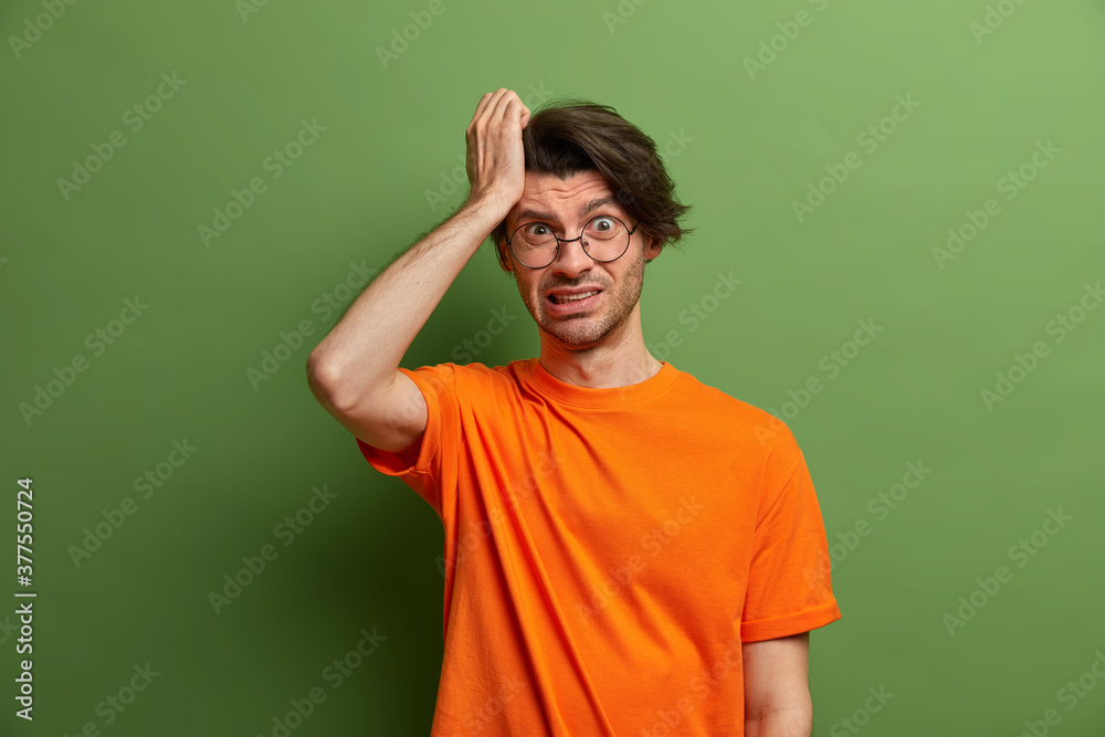 Stressed frustrated man touches head and feels miserable pain. Discontent tired student clenches teeth because of headache, needs painkillers. Male in round spectacles suffers terrible migraine Stressed frustrated man touches head and feels miserable pain. Discontent tired student clenches teeth because of headache, needs painkillers. Male in round spectacles suffers terrible migraine