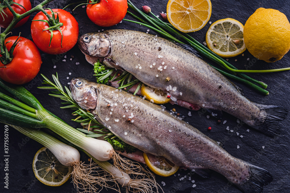 fresh rainbow fish trout on black stone background with vegetables fresh rainbow fish trout on black stone background with vegetables