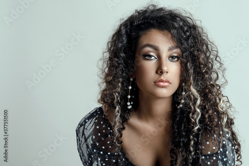 Portrait of beautiful girl model with makeup and long dark curly hair.