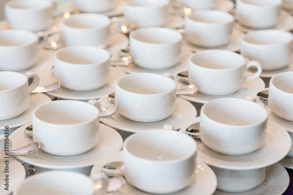 Rows of clean white coffee or tea cups, dish and spoon in a cafeteria or restaurant ready to serve a hot beverage Rows of clean white coffee or tea cups, dish and spoon in a cafeteria or restaurant ready to serve a hot beverage