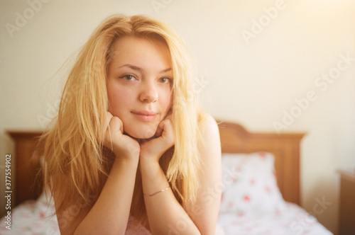 Young caucasian woman waking up in the bedroom early in the morning. Young woman sitting near a double bed in the morning. The real grain of the scanned film.