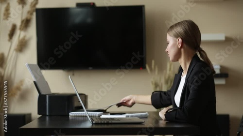 Beautiful caucasian woman taking printed documents from a printer. Workplace at home.