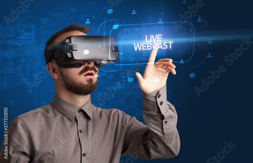 Businessman looking through Virtual Reality glasses with LIVE WEBCAST inscription, social networking concept