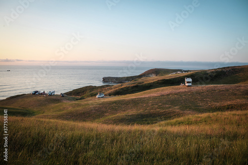 camper vans and caravans on the top of the cliff under the Atlantic ocean, golden light through beautiful sunset in the North Spain, Cantabria, large meadow