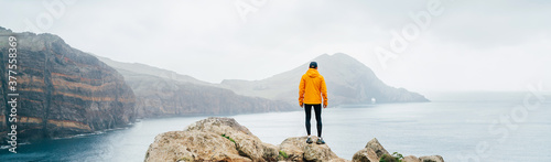 Trail runner man dressed orange waterproof jacket, running tights and shoes enjoying Atlantic ocean bay view on Ponta de Sao Lourenço peninsula -the easternmost point of Madeira island, Portugal
