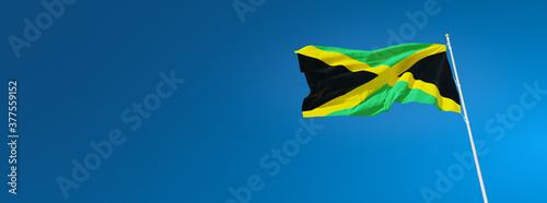 The beautiful flag of Jamaica waving against a blue sky in wide format. Jamaican national flag on background