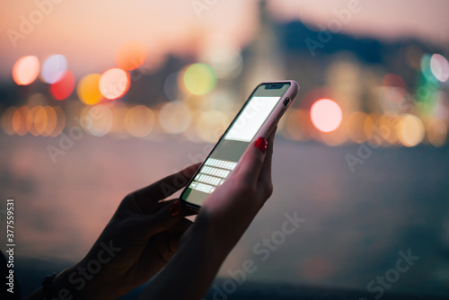 Smartphone with blank screen in female hands on blurred night city background