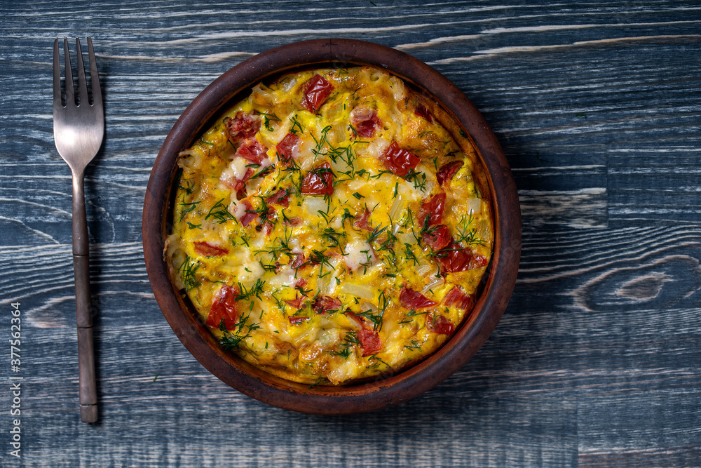 Ceramic bowl with vegetable frittata, simple vegetarian food. Frittata with tomato, pepper, onion and cheese on wooden table, close up
