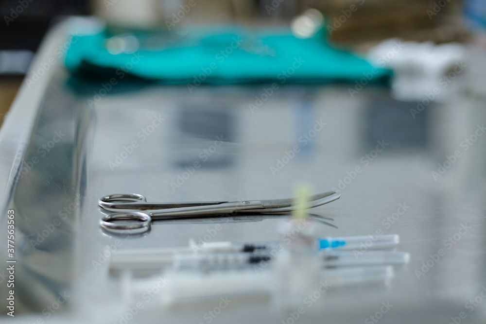 Curved surgical scissors on operation table in veterinary clinic, with couple of syringes in out of focus foreground. Close up, side view.
