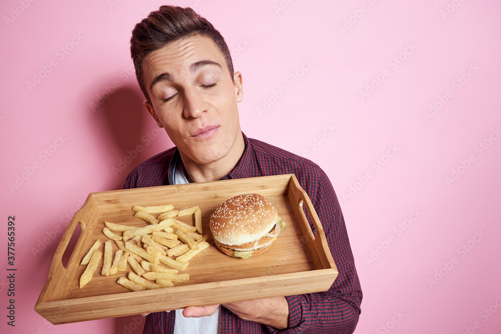 Man with fast food eating hamburger french fries pink background Man with fast food eating hamburger french fries pink background