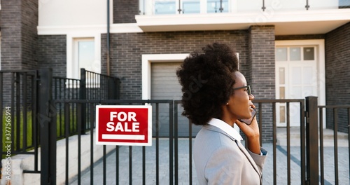 Foto African American young stylish female real-estate agent at suburb street and talking on mobile phone