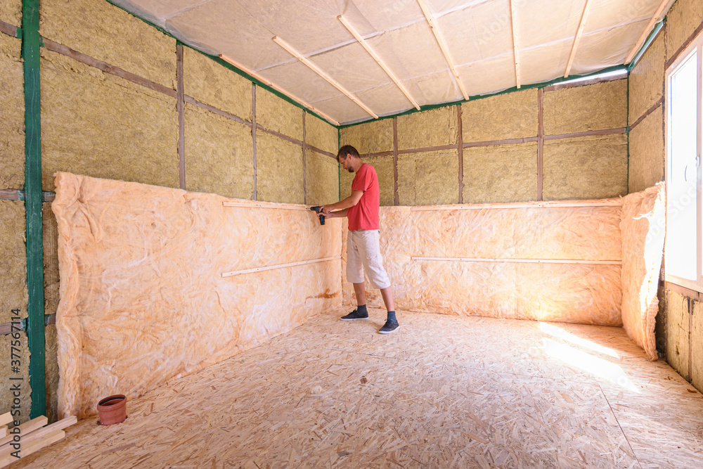 A worker is installing a roll of insulation in the construction of a country house A worker is installing a roll of insulation in the construction of a country house
