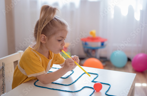 Little girl enjoying game playdough straw maze. Great activity for building oral motor skills at home. photo