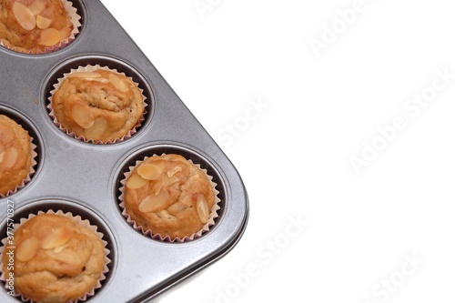 In selective focus homemade banana muffins in a black baking tray with almond sliced on top,on white isolated background with copy space