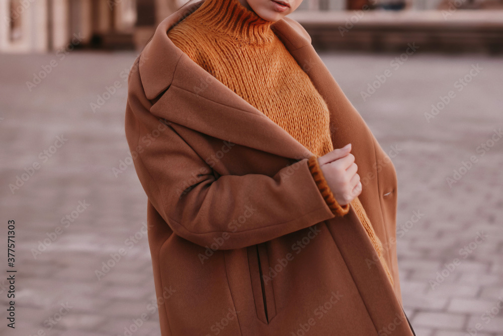 Young woman  with cropped face in an orange knitted sweater and brown coat outdoor portrait in daylight. Cozy autumn fashion style.  - obrazy, fototapety, plakaty 